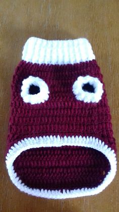 a crocheted red and white hat with googly eyes on the top, sitting on a wooden surface