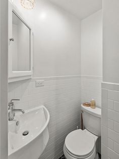 a white toilet sitting next to a sink in a bathroom under a light hanging above it