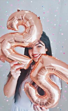 a woman holding two large gold balloons in front of her face with the number six on it