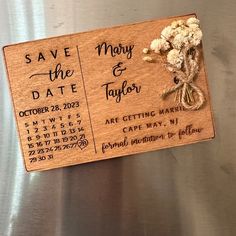 a wooden save the date magnet with dried flowers on it, attached to a stainless steel refrigerator