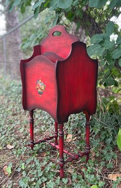 a red wooden stand with two drawers on it's legs in the grass next to some trees