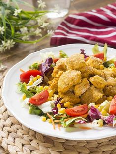 a white plate topped with fried food next to a basket filled with vegetables and corn