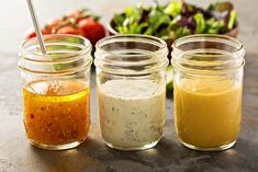 four jars filled with different colored sauces on top of a table next to a salad