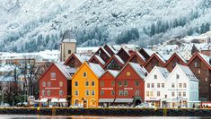 the colorful houses are along the water's edge with mountains in the background and snow on the ground