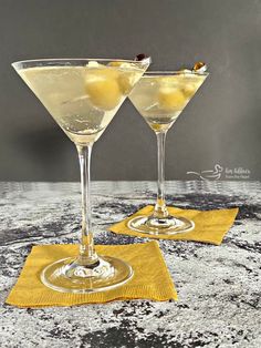 two martini glasses with lemon garnish sit on a yellow napkin next to each other