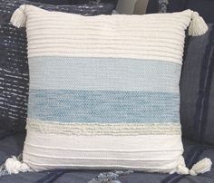 a blue and white striped pillow with tassels on the sides sitting on a bed