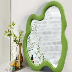 a green mirror sitting on top of a counter next to a vase and potted plant