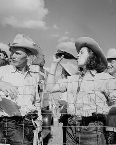 black and white photograph of three men in cowboy hats standing behind a barbed wire fence