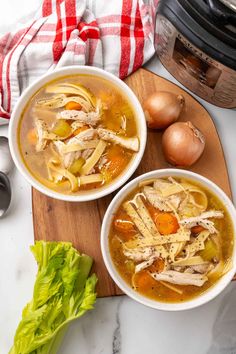 two bowls of chicken noodle soup on a cutting board