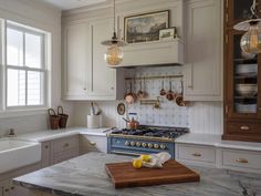 a kitchen with marble counter tops and white cabinets, an island in the middle is surrounded by hanging lights