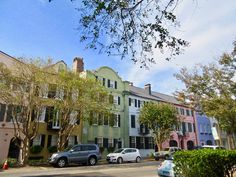 cars parked on the side of a street in front of multi - colored buildings and trees