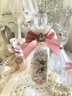 a glass bottle with pink flowers and pearls on it sitting on a lace tablecloth