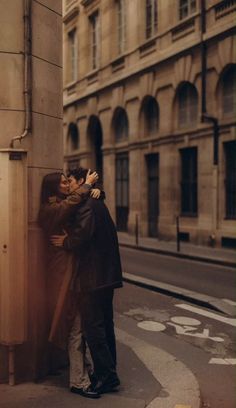 two people standing next to each other near a building and one is hugging the other