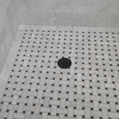 a black and white tiled shower with a drain on the floor in front of it