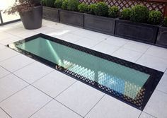 a glass floor in the middle of a patio with potted plants behind it and a black metal grate on the ground