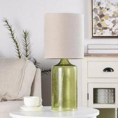 a green vase sitting on top of a table next to a lamp