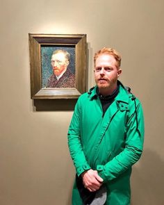 a man is standing in front of a painting and looking at the camera with his hands on his hips