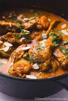 chicken curry with almonds and cilantro served in a black bowl on a white surface