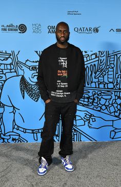 a man standing in front of a blue and black wall with his hands in his pockets