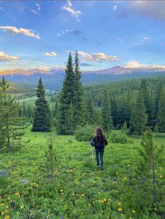 a woman walking through a lush green field with mountains in the backgrouund