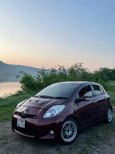 a small car parked on the side of a dirt road near a body of water