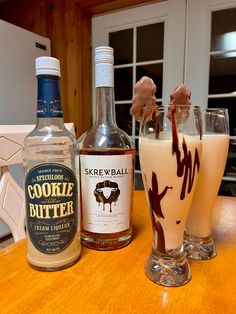 two glasses filled with ice cream next to bottles of booze and chocolate on a table