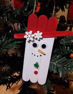 a snowman ornament hanging from a christmas tree with pine cones and branches