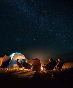 people sitting in chairs around a campfire under the night sky with stars above them