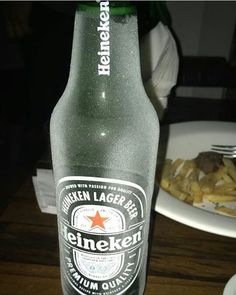 a bottle of beer sitting on top of a wooden table next to a plate of food