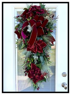 a christmas wreath with red flowers and greenery hangs on the front door's glass door