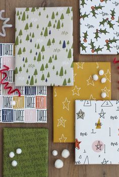 christmas cards laid out on a wooden table with white and green wrapping paper next to them