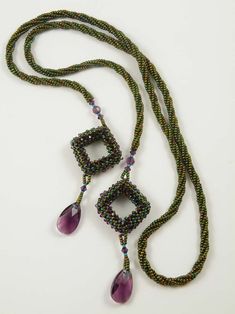 a long necklace with two pendants hanging from it's sides on a white surface