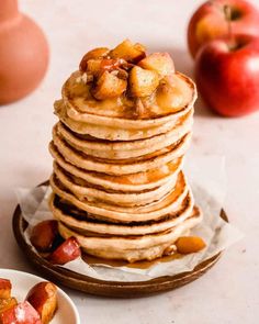 a stack of pancakes with apples and nuts on the top, next to two bowls of fruit