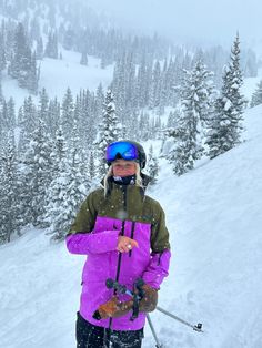 a person on skis standing in the snow with trees behind them and wearing a purple jacket