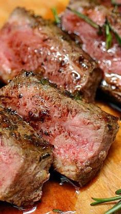 some meat is sitting on a cutting board with rosemary sprigs around the steak