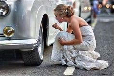 a woman kneeling down in front of a white car eating something out of her hand