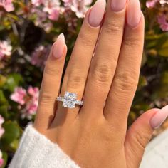 a woman's hand with a ring on it and pink flowers in the background