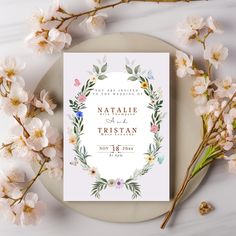 a wedding card with flowers and leaves on it next to some white flowers in the background