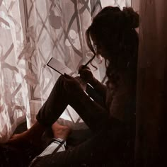 a woman sitting in front of a window writing on a piece of paper while holding a pen