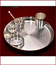 a metal tray with silver cups and spoons on it, sitting on a red table