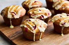 there are many muffins with icing on the wooden board and one has cranberries in it