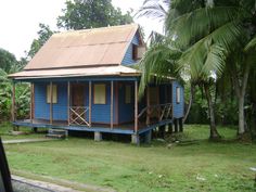 a small blue house sitting in the middle of a lush green field next to trees