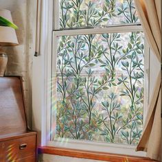 a window with leaves drawn on it in front of a wooden dresser and side table