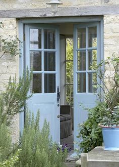 an open door to a stone building with potted plants in the front and side