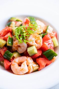 a white bowl filled with shrimp, cucumber and tomato salad on top of a table