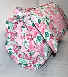 a pink and green floral bag sitting on top of a white floor next to a wall