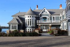 a large gray house sitting on top of a brick road next to a body of water