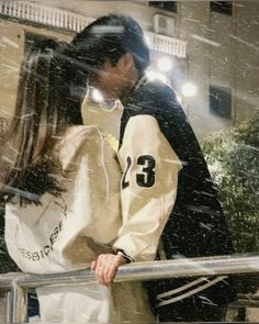 a man and woman standing next to each other on a balcony in the snow with buildings behind them