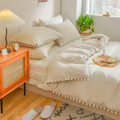 a bed with white comforter and pillows in a bedroom next to a lamp on a table