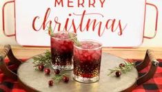 two glasses filled with red liquid sitting on top of a tray next to a merry christmas sign